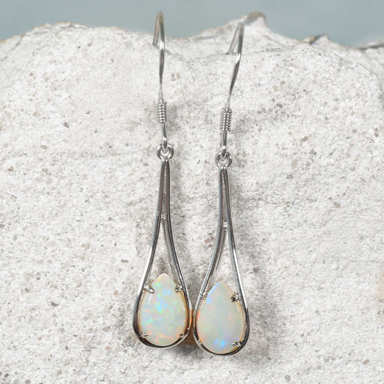 Teardrop-shaped opal earrings on a textured white surface