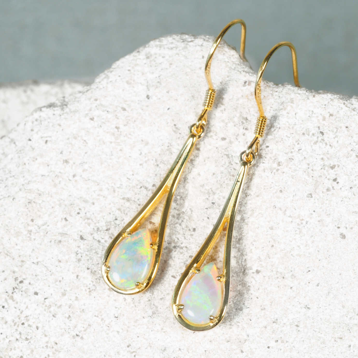 Gold teardrop earrings with opal stones on a textured surface