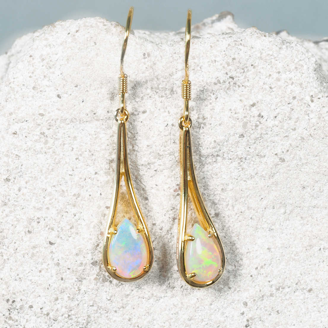 Gold teardrop earrings with opal stones on a textured white surface