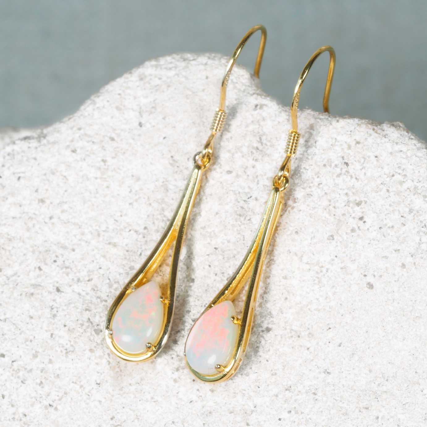Gold earrings with opal stones on a textured surface