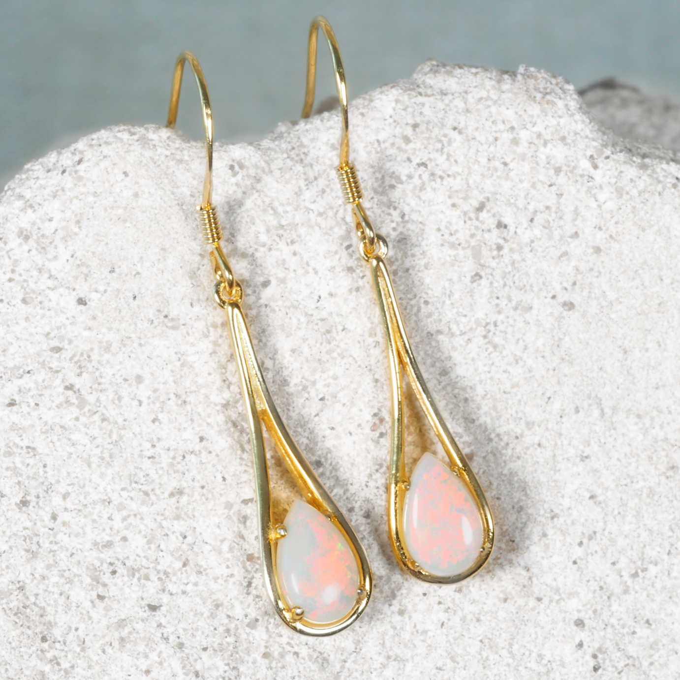 Gold earrings with pink opal stones on a textured surface