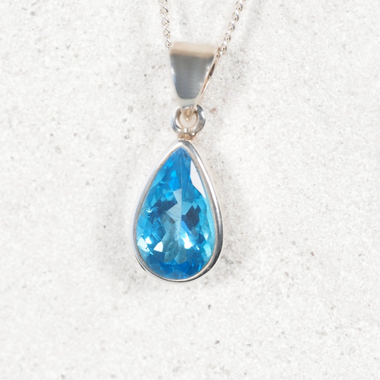 blue topaz pendant displayed in a silver frame bezel setting
