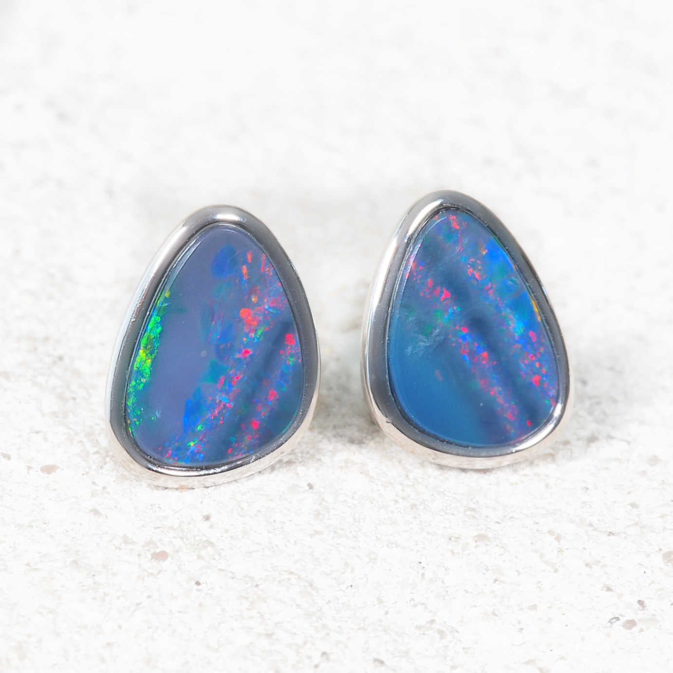 Teardrop-shaped opal earrings with colorful interior on a textured white background