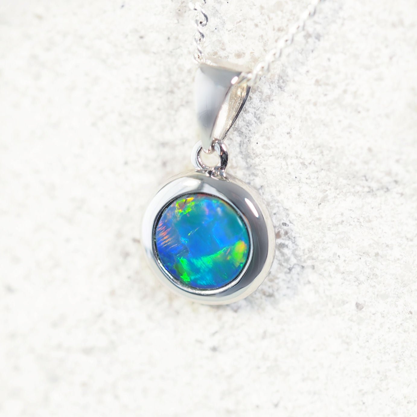 Round Australian doublet opal pendant showing vibrant blue base and rainbow colour flashes in white gold setting