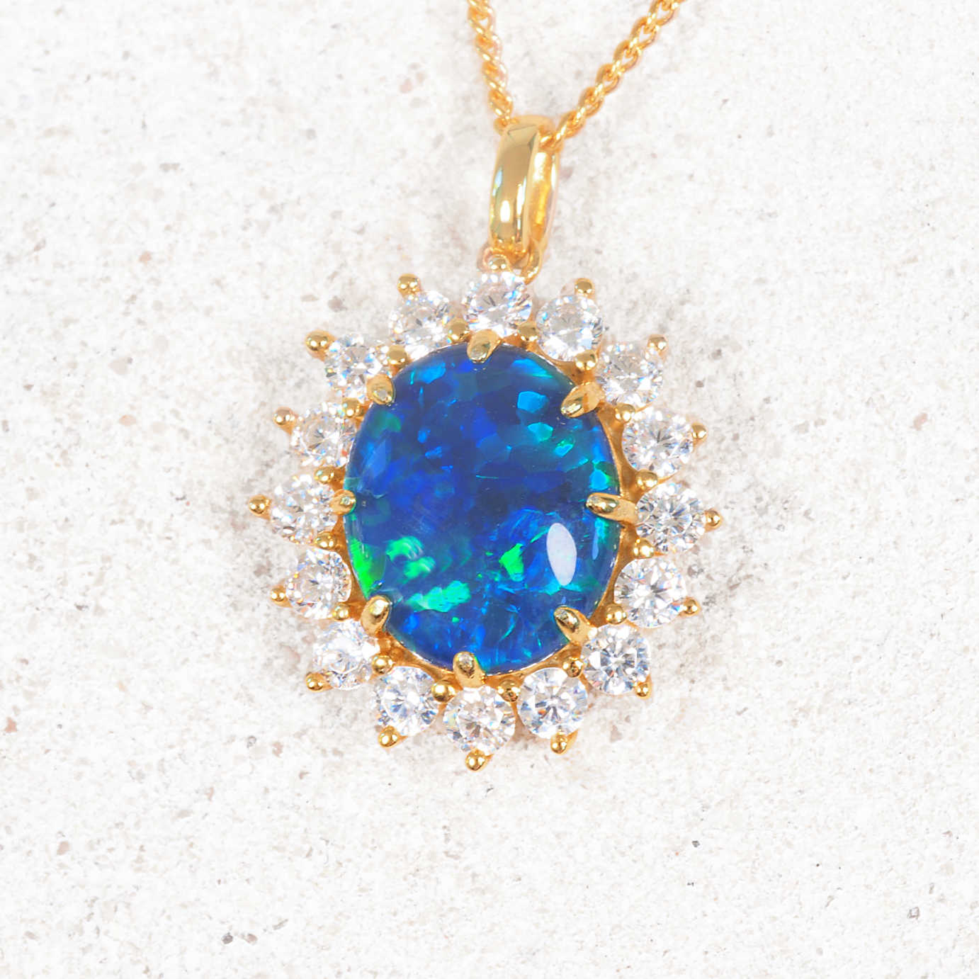 Gold pendant with a blue gemstone and clear stones on a white background