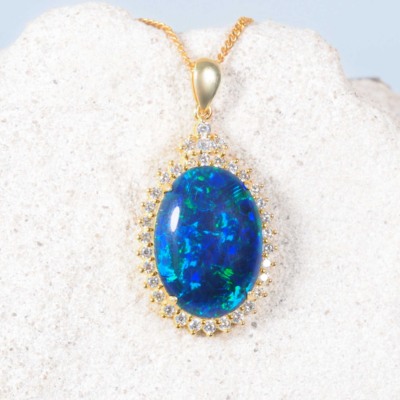 Blue opal pendant with gold frame on a white sand background
