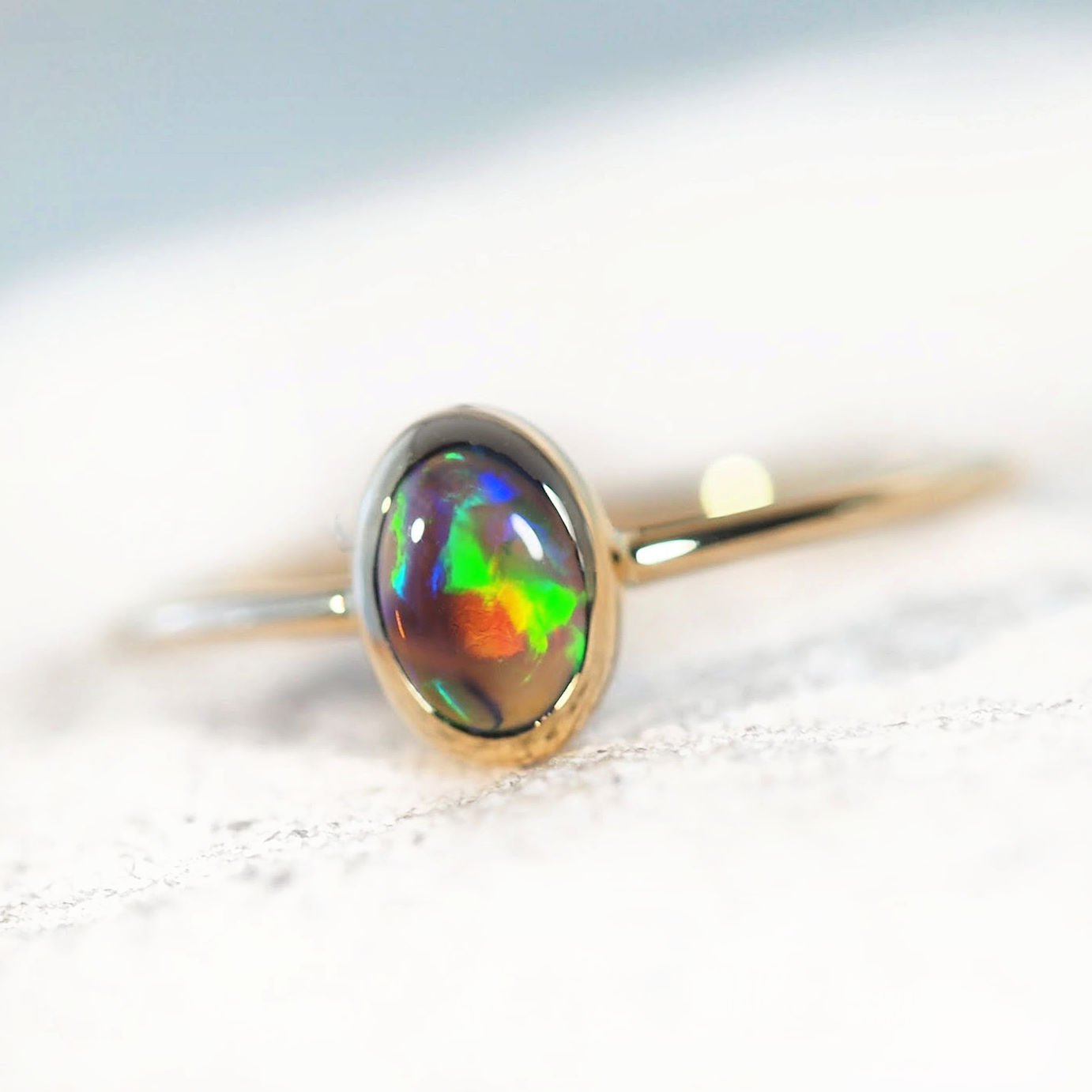 Gold ring with a colorful opal stone on a light background