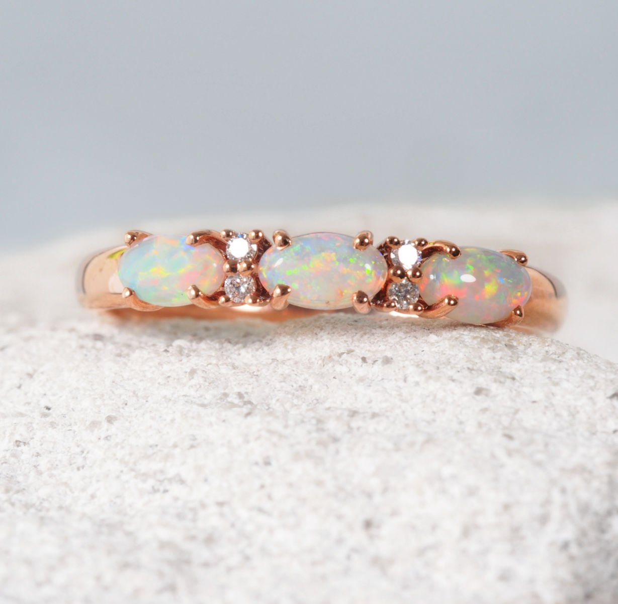 Rose gold ring with opal stones on a textured surface