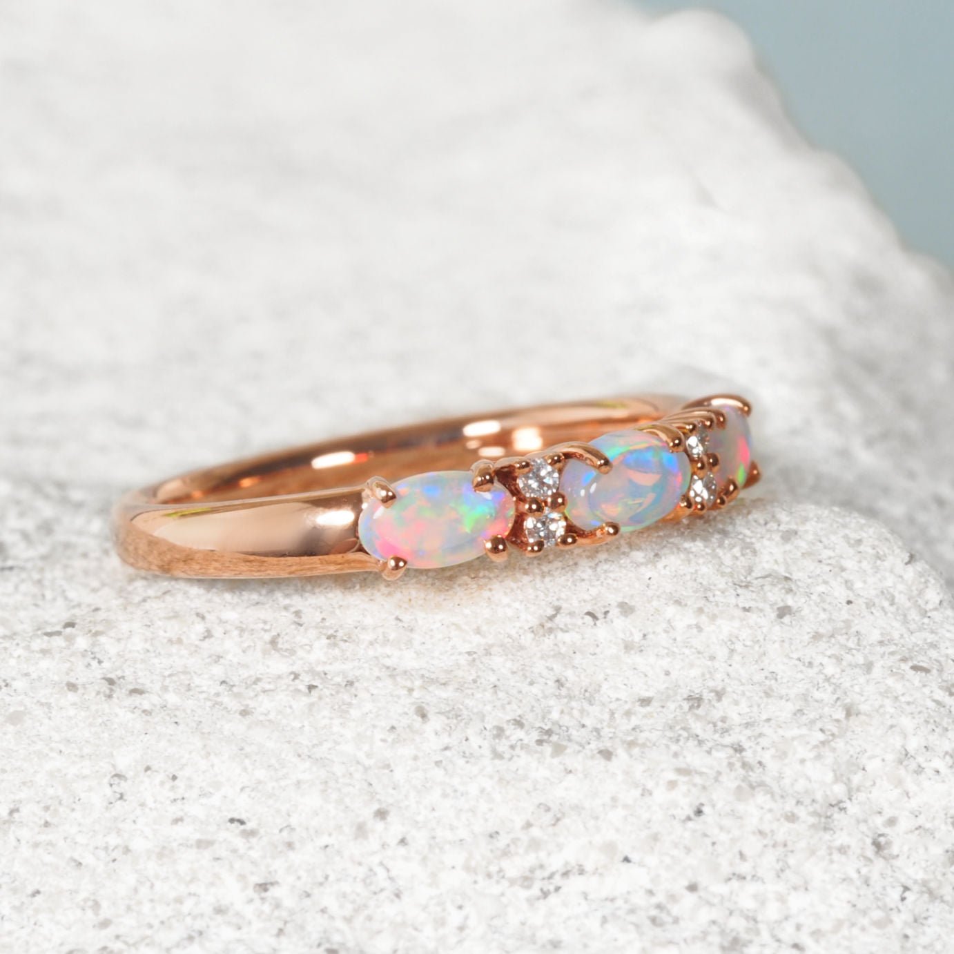 Rose gold ring with opal stones on a textured surface