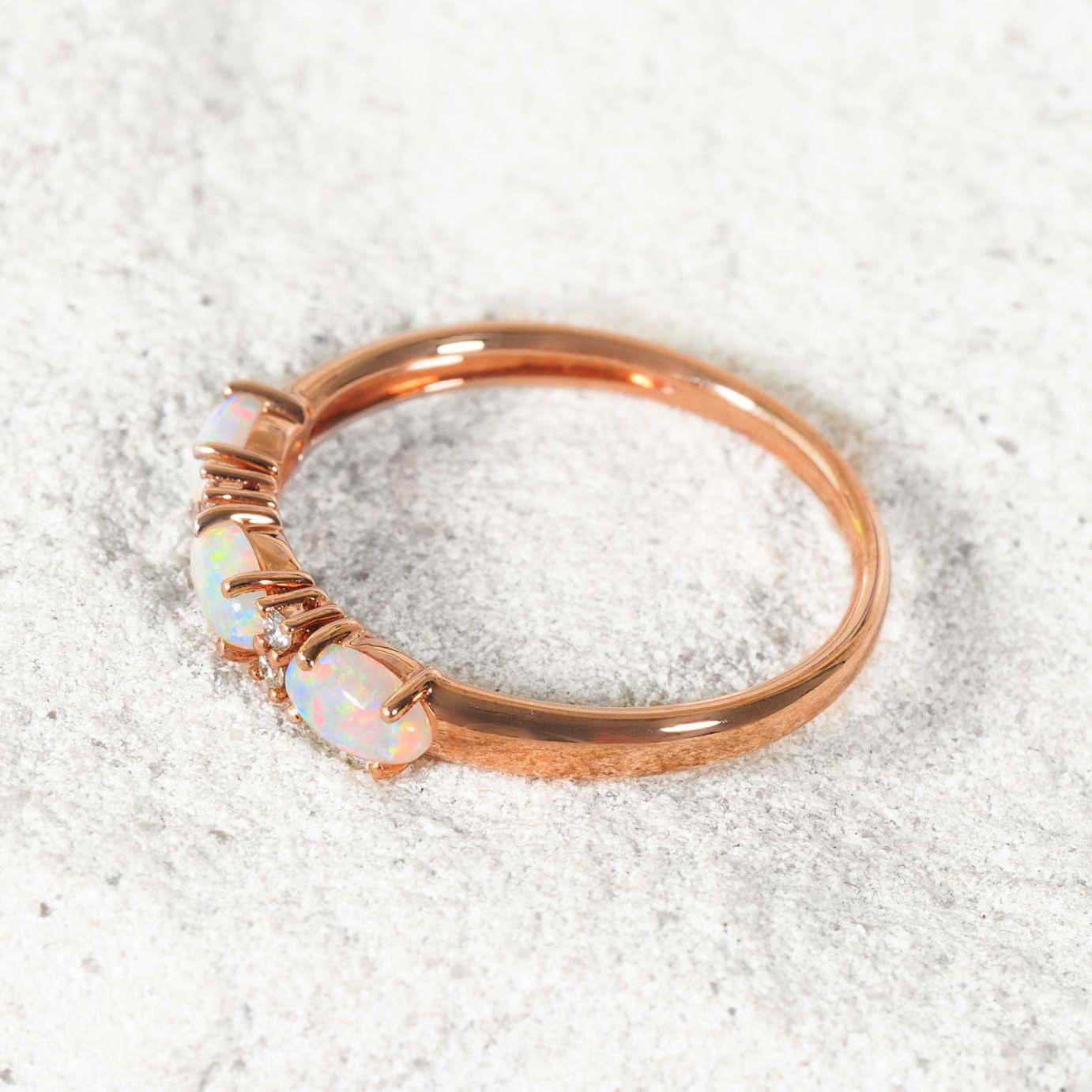 Rose gold ring with opal stones on a white sand background