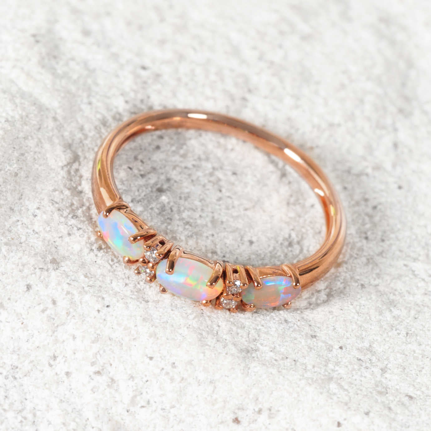 Rose gold opal ring with opal stones on a textured white background