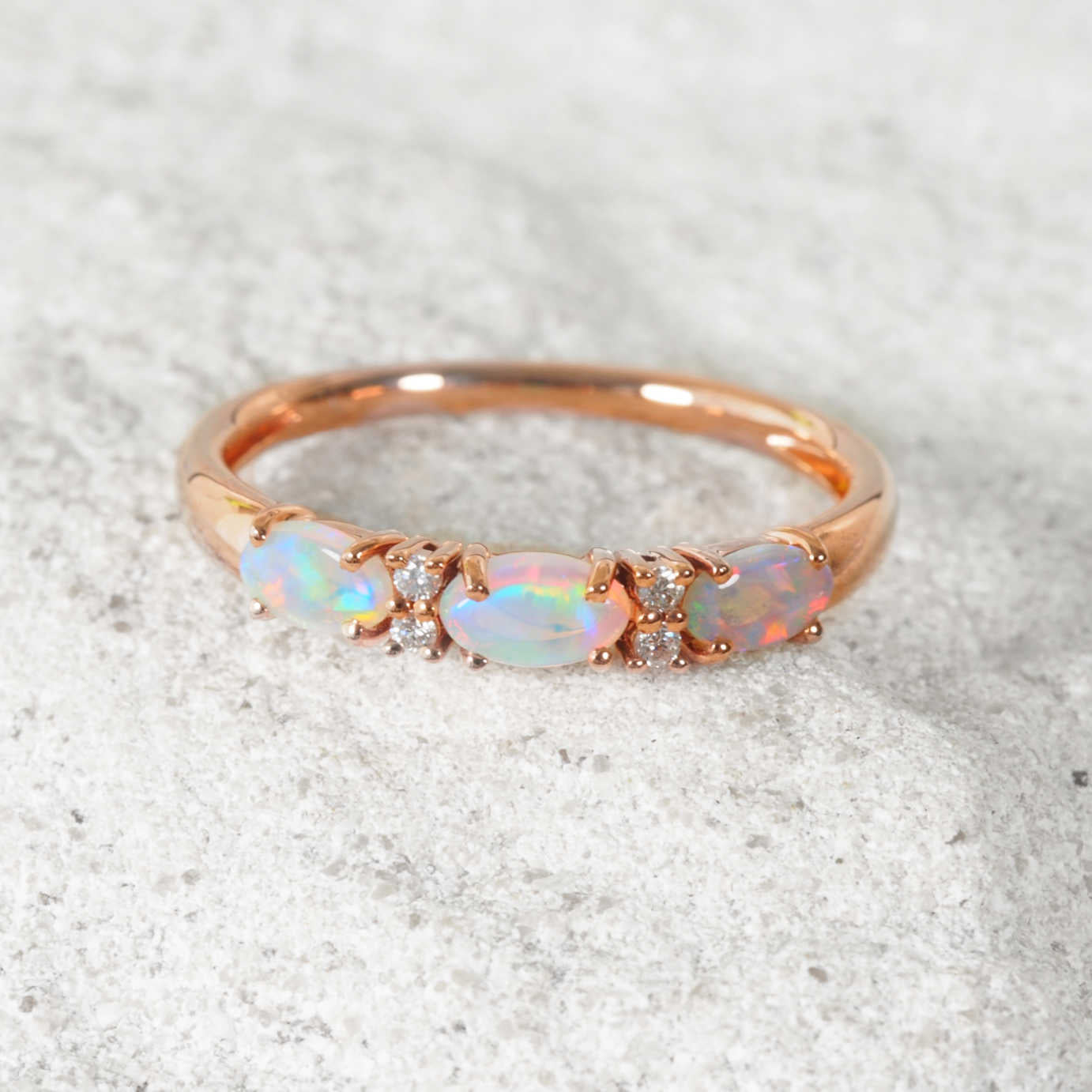 Rose gold ring with opal stones on a textured gray background