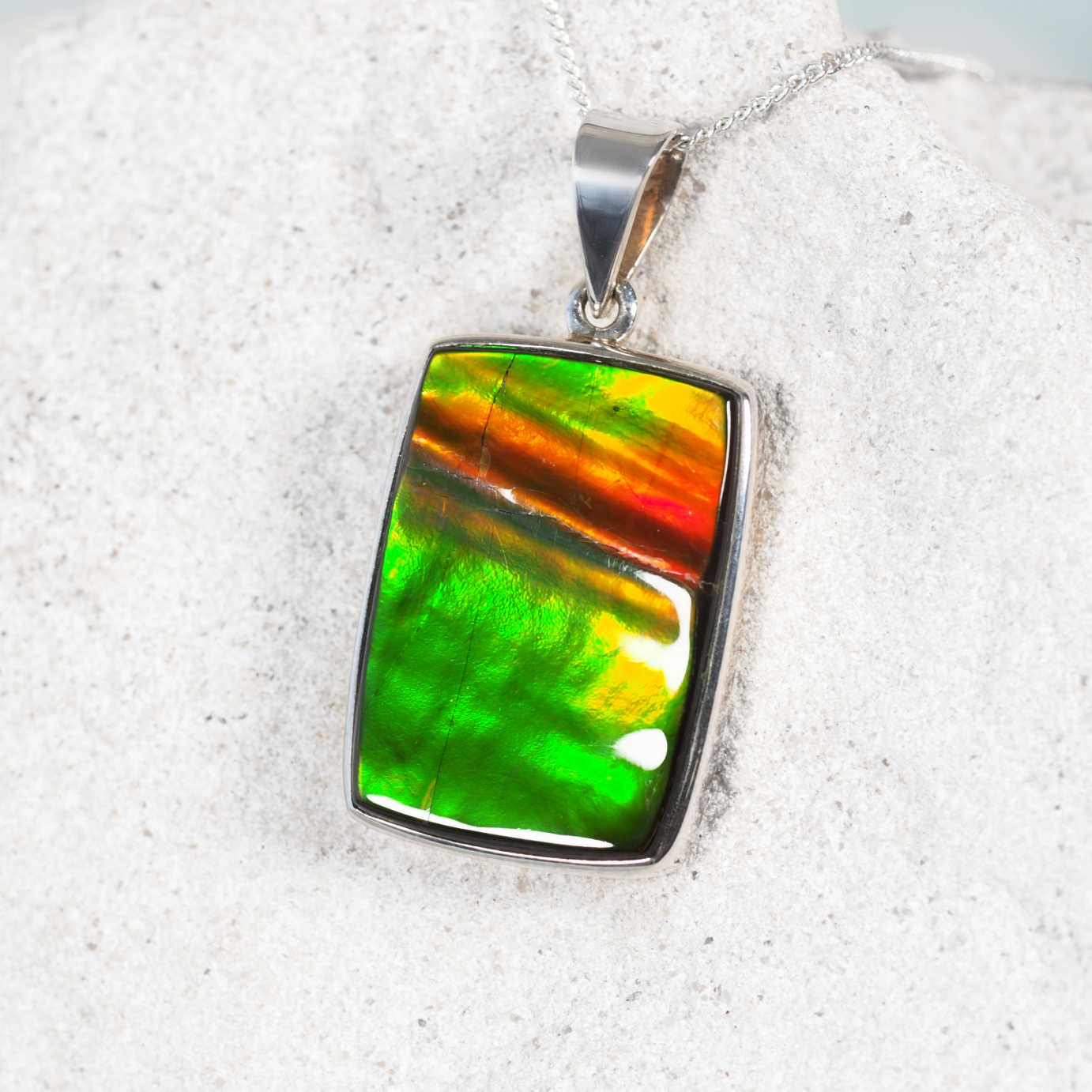 Close-up of 'Rylee' pendant showing the luminous Ammolite gemstone in a sleek silver setting with rich fiery and green tones