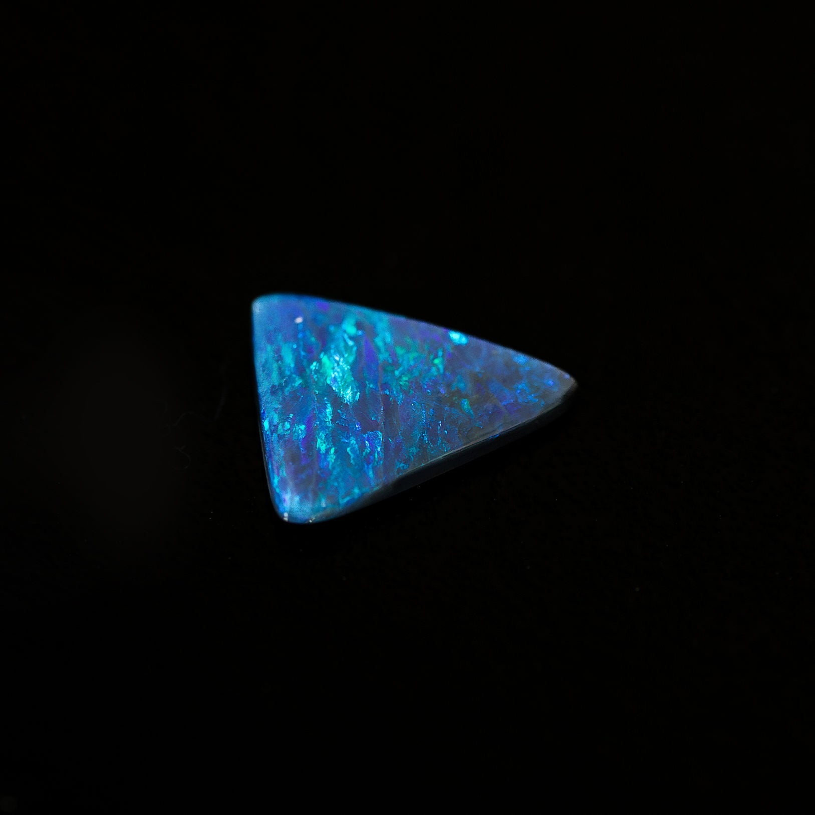 Hand-cut triangular black opal gemstone showcasing vivid oceanic blues and lush greens