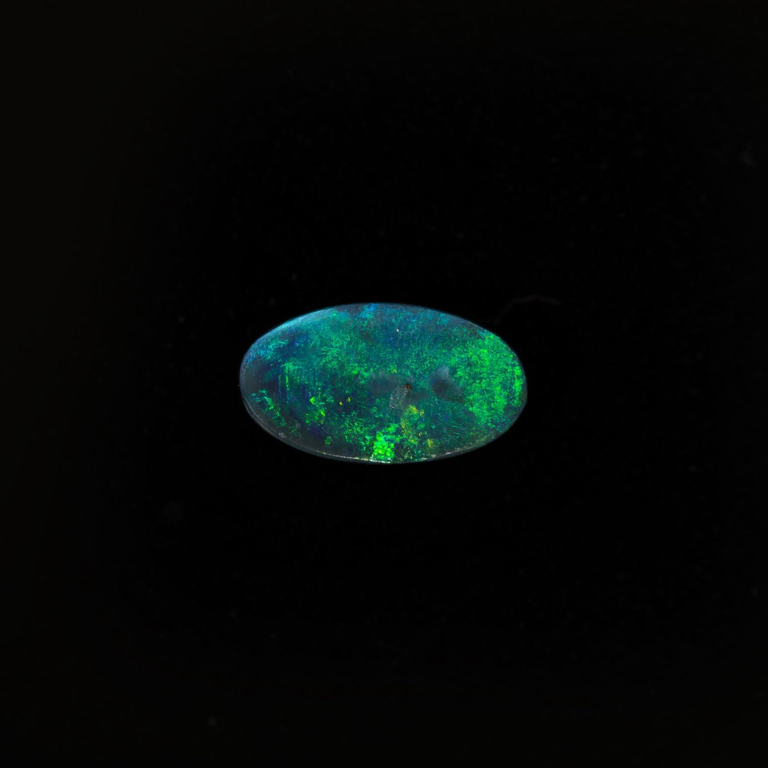 Oval-shaped black opal with vibrant green speckles from Lightning Ridge, showcasing a deep midnight body tone