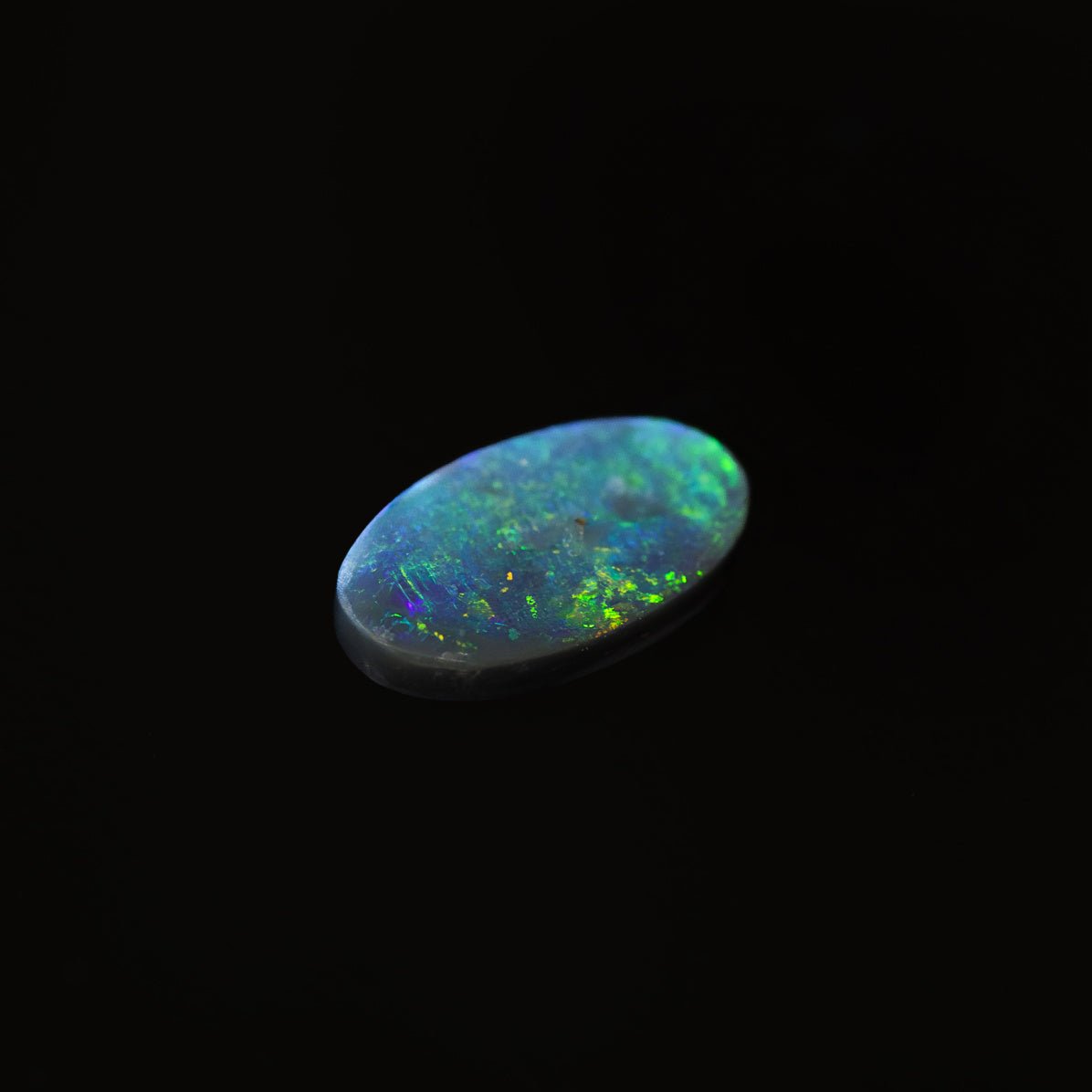 Close-up of Shadowfern black opal, displaying vivid green hues and a smooth oval shape.