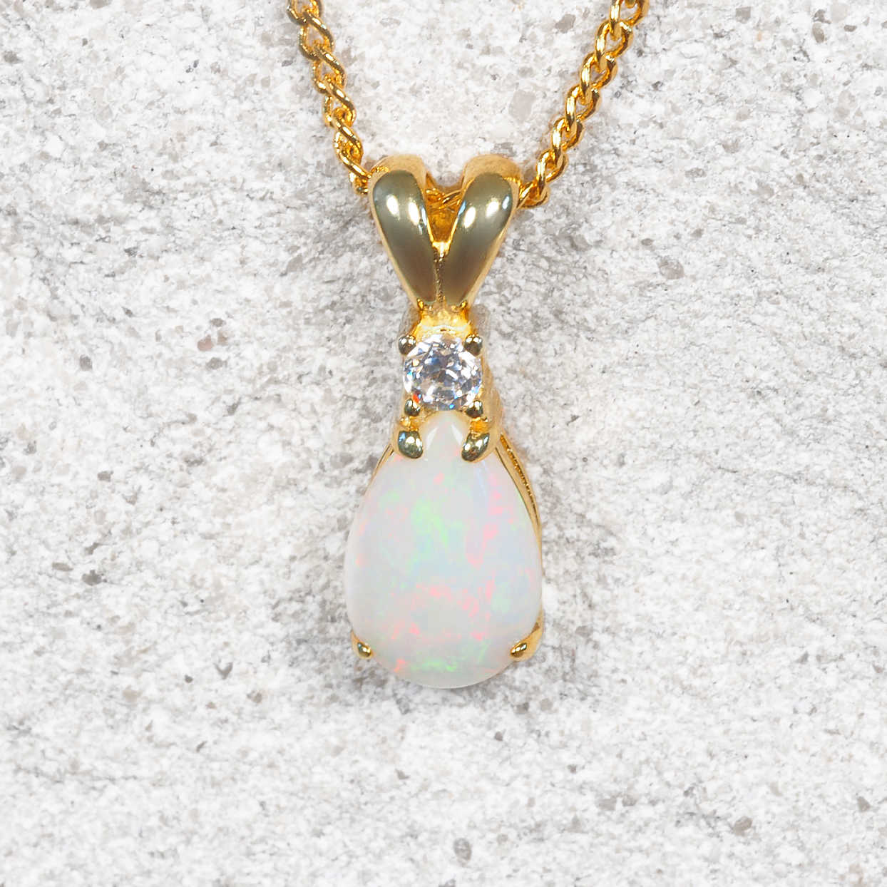 Gold necklace with a teardrop-shaped opal stone on a textured white background