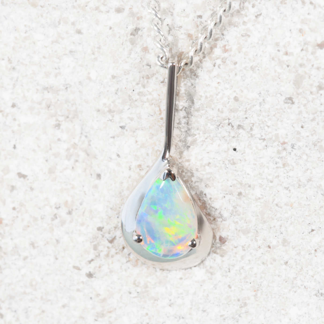 Teardrop-shaped opal pendant on a silver chain against a light background
