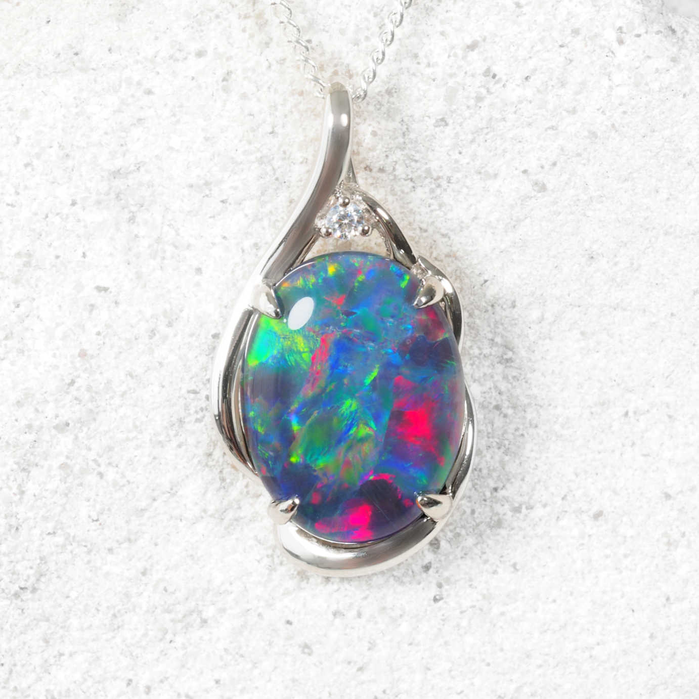 Colourful opal pendant with silver setting on a textured white background