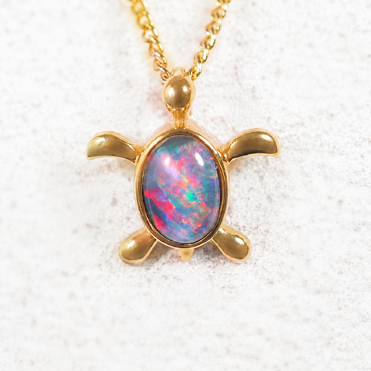 Gold turtle pendant with an opal stone on a white background