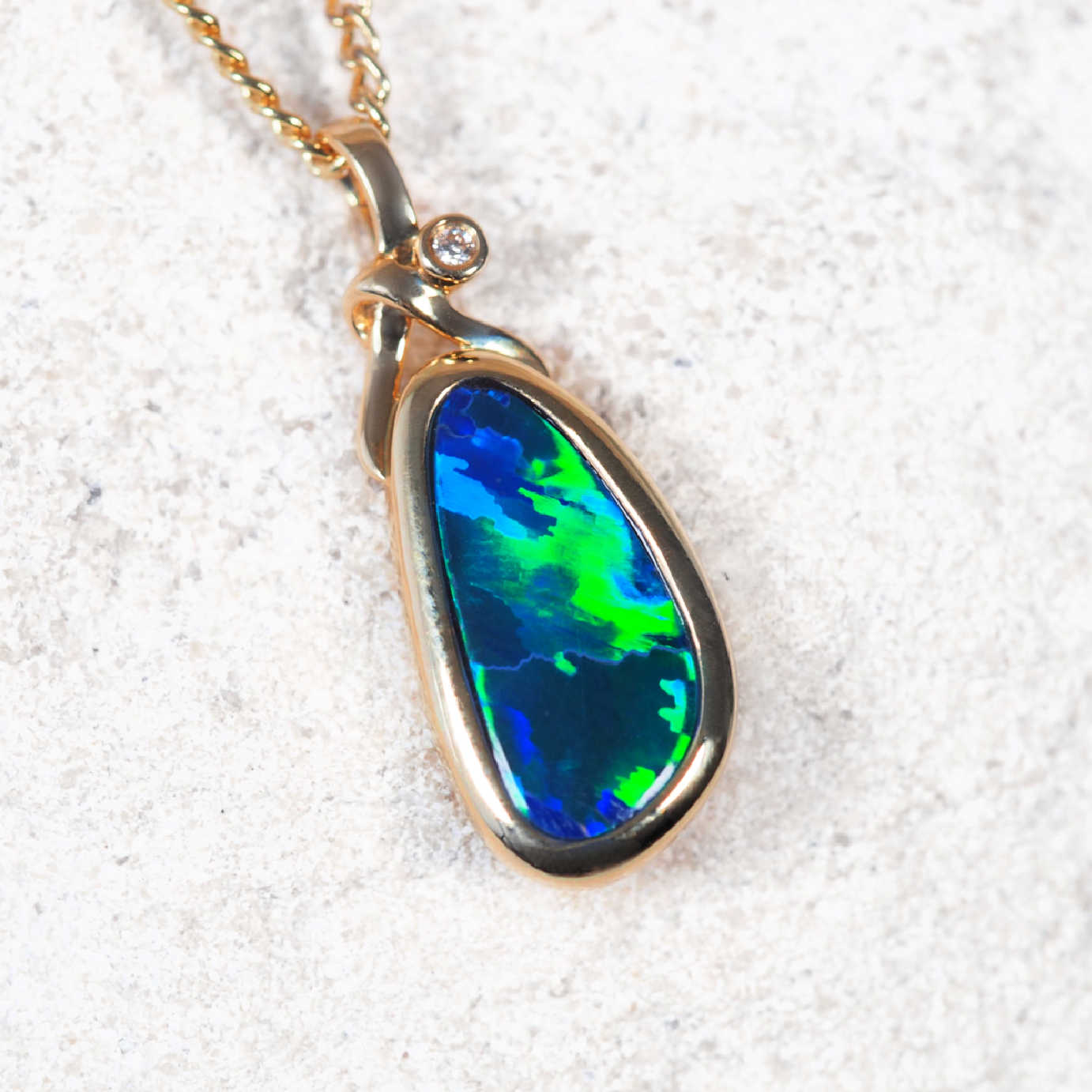 Opal pendant on a gold chain against a white sand background